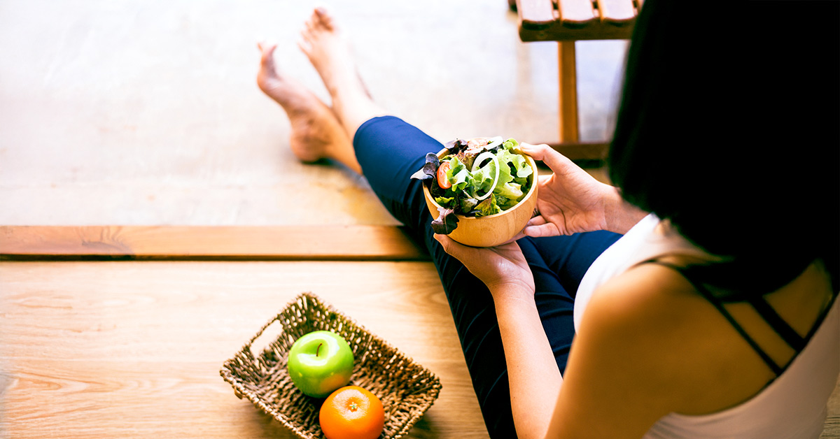 Woman sitting on the floor in leggings holding a salad bowl