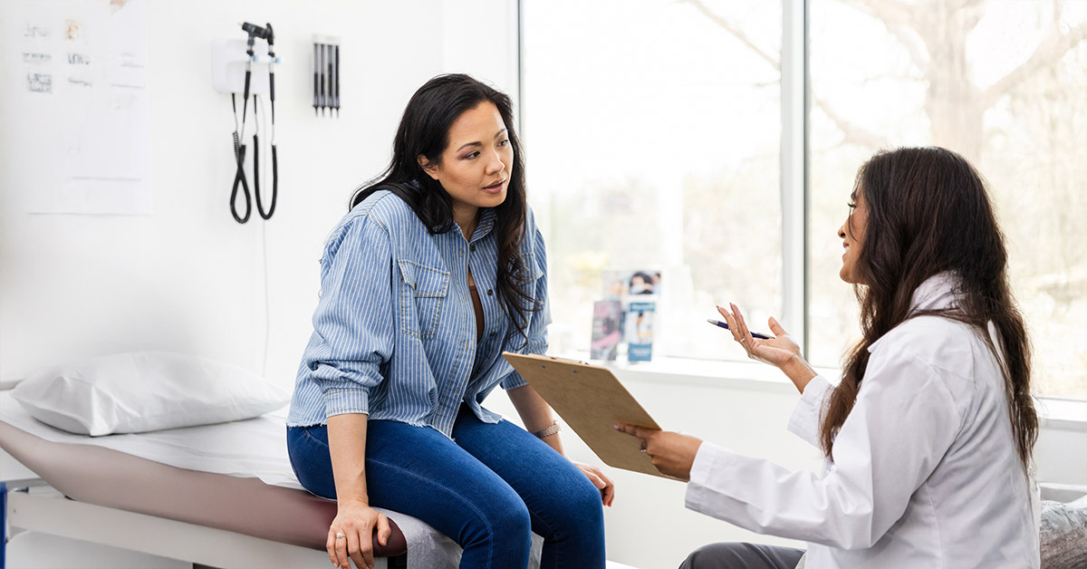 Woman sitting on an exam table discussing a planned procedure with a healthcare provider.