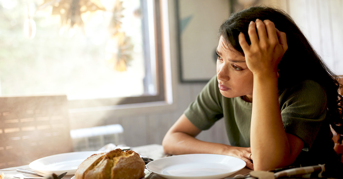 A woman not enjoying sitting at the table with food.