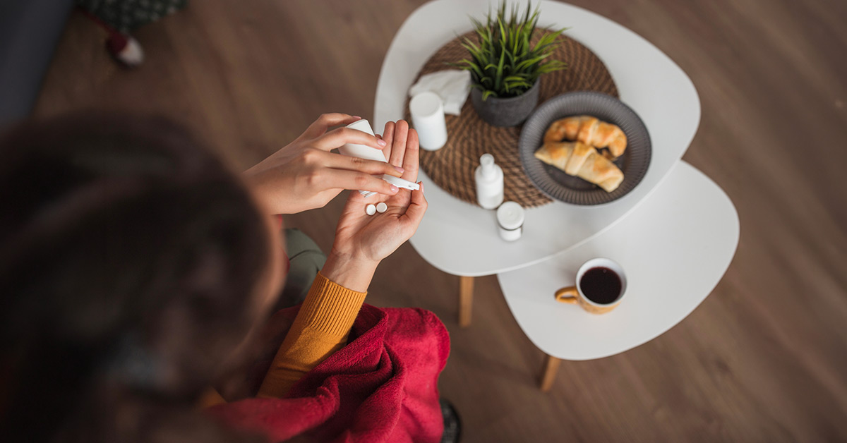 Woman with croissants and coffee examining her medication. 