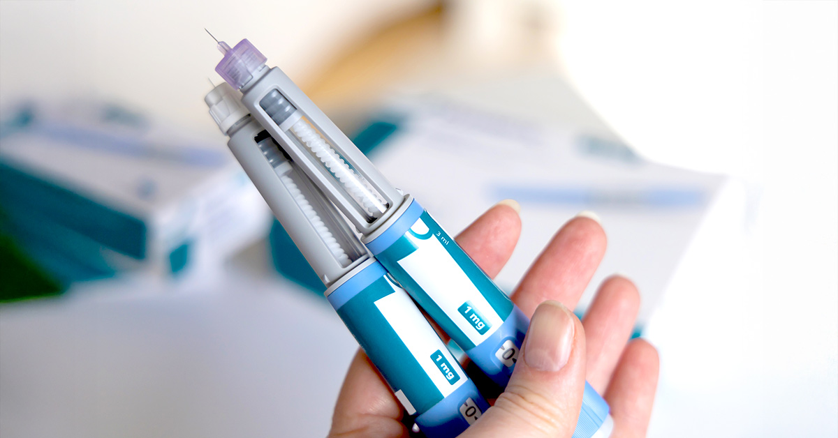 A person holding two semaglutide injection pens in their hand above packaging.