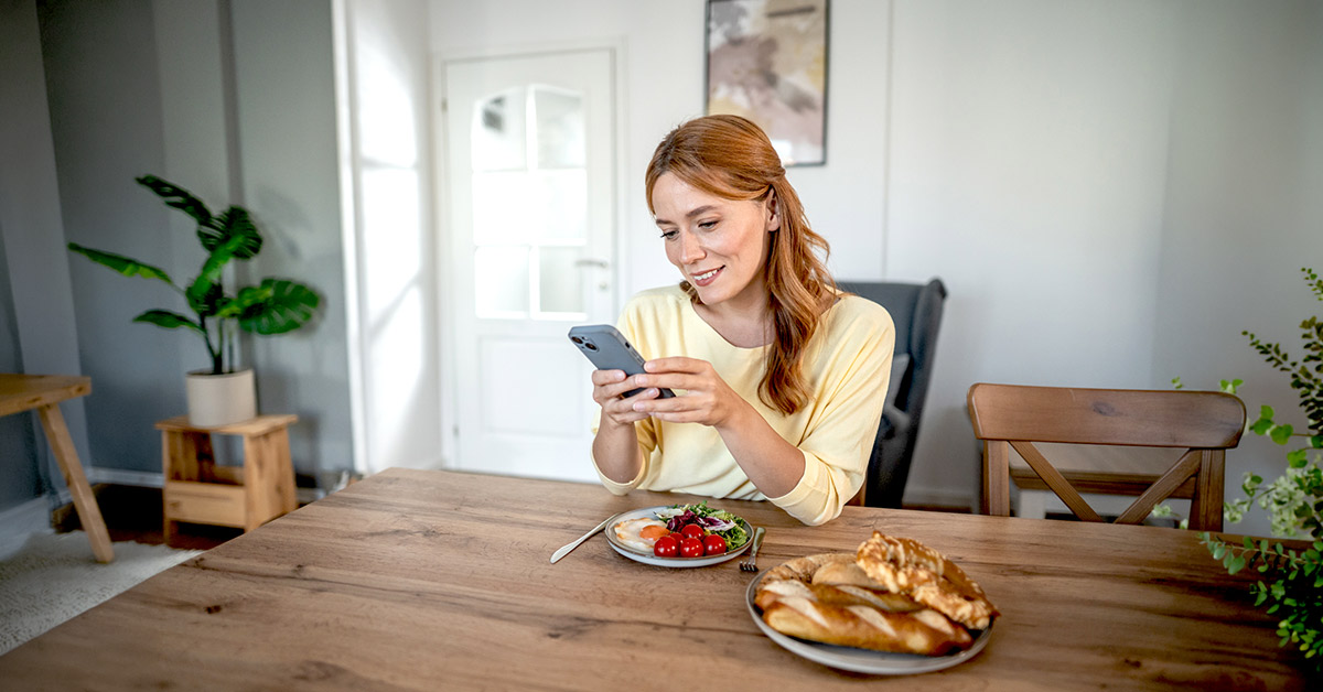 A calm and happy woman looking into her phone at the table with breakfast