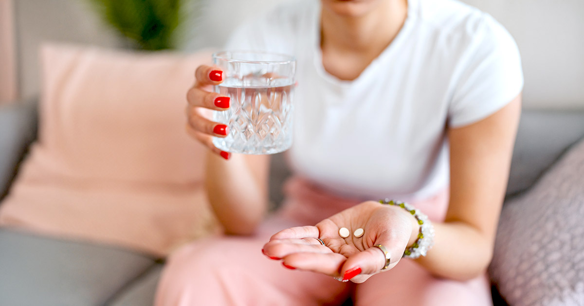 A woman holding oral medication in her hand with a glass of water in the other. 
