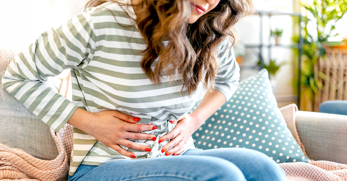 A woman holding onto her stomach while sitting due to GI discomfort
