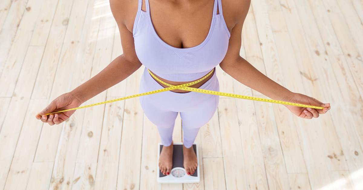 A woman in fitness class standing on top of scale with a yellow measuring tape around her waist