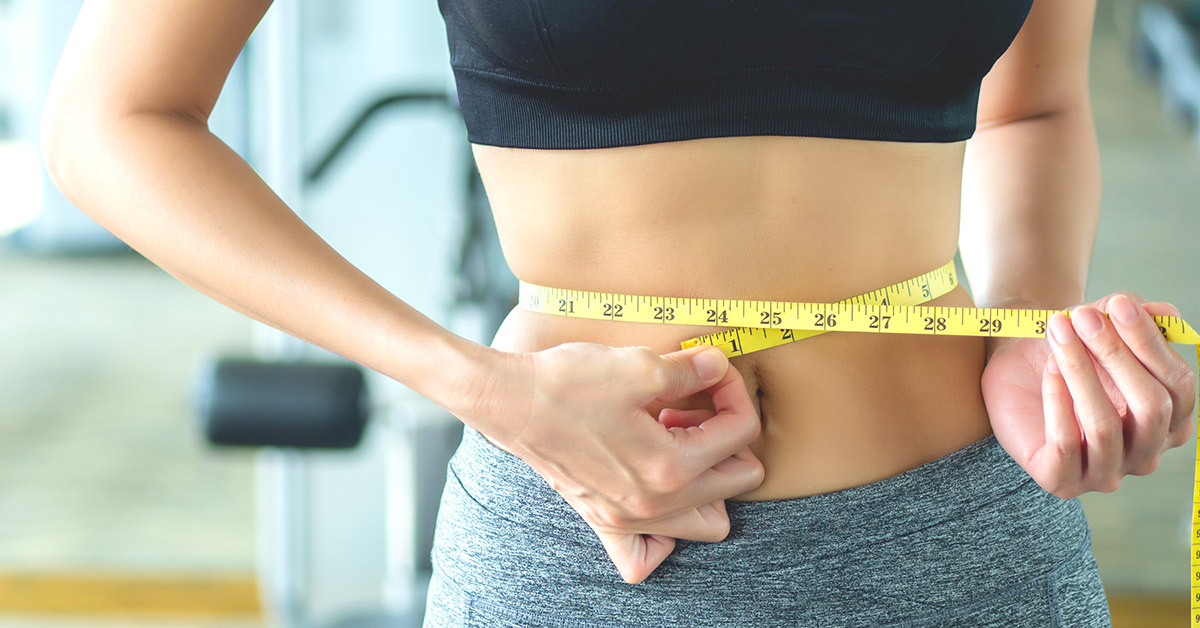 A woman measuring her waist size with a yellow tape measure