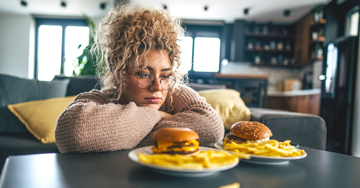 A woman staring at two plates of burgers and fries on her coffee table. 