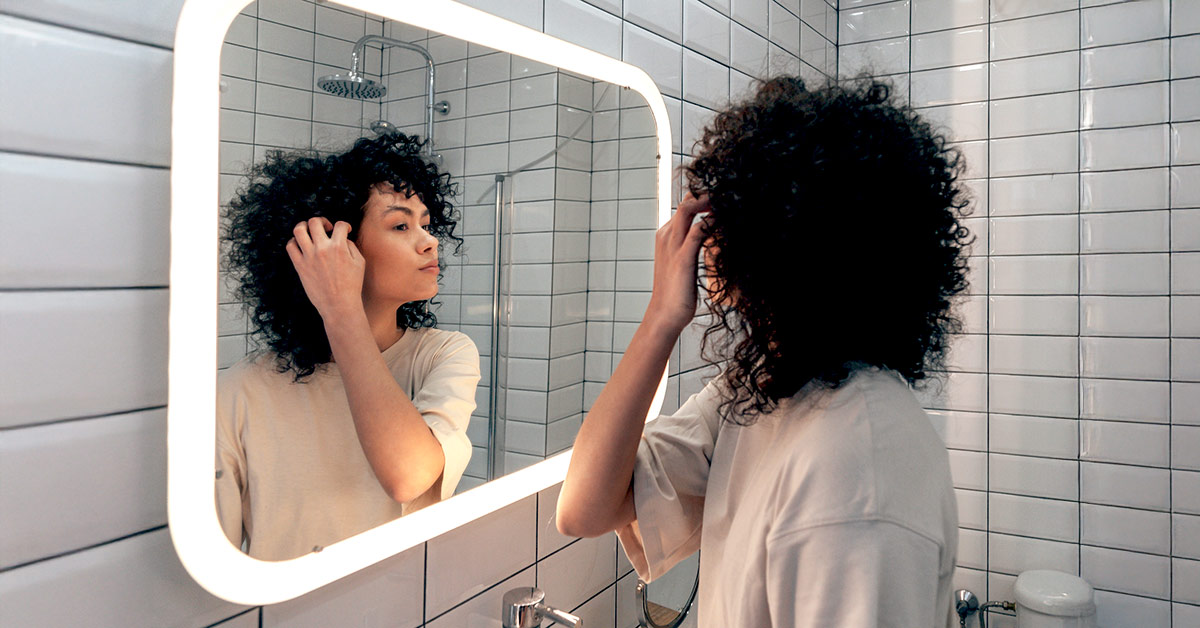 A woman examining her hair in her bathroom through a mirror