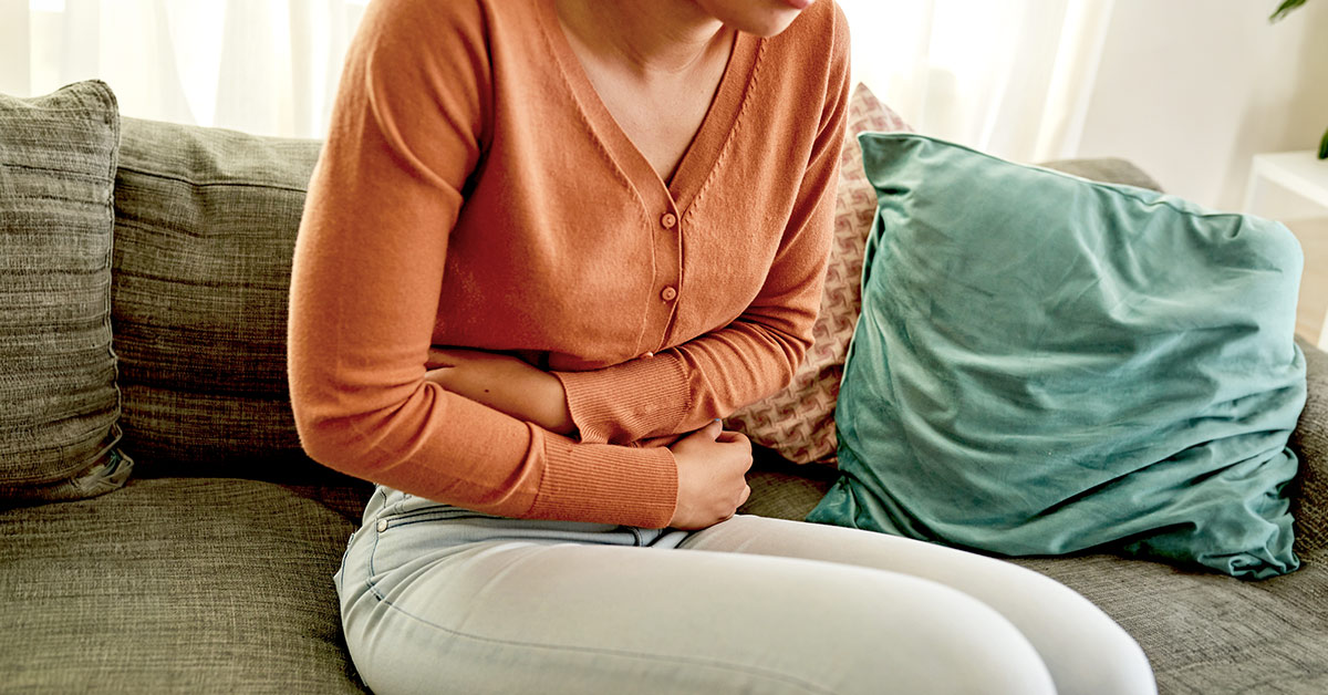 A woman sitting on the sofa at home holding her stomach experiencing pain