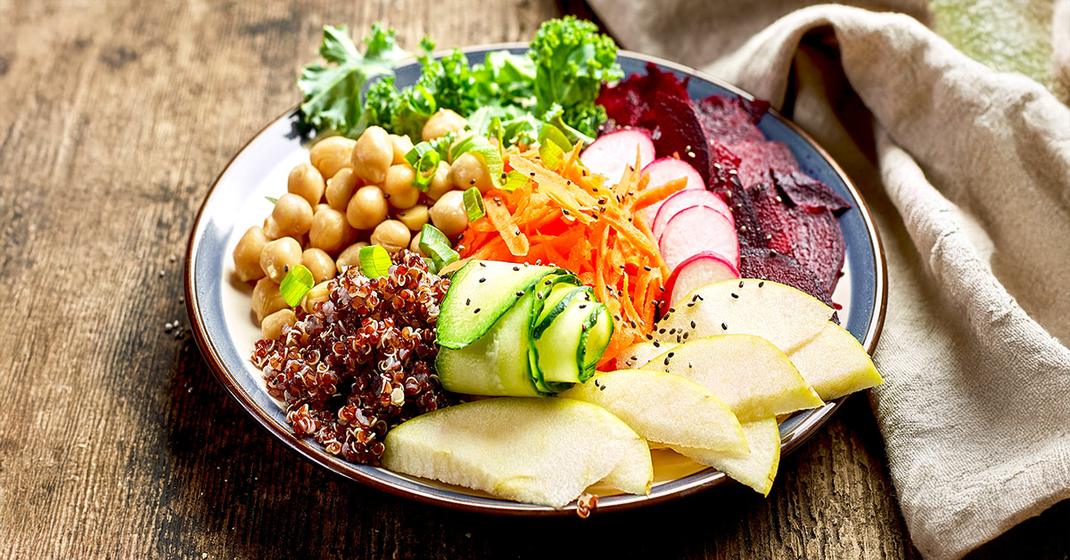 A nutritious meal consisting of apples, cucumbers, chickpeas, and more, nicely placed on a plate on a wooden table. 