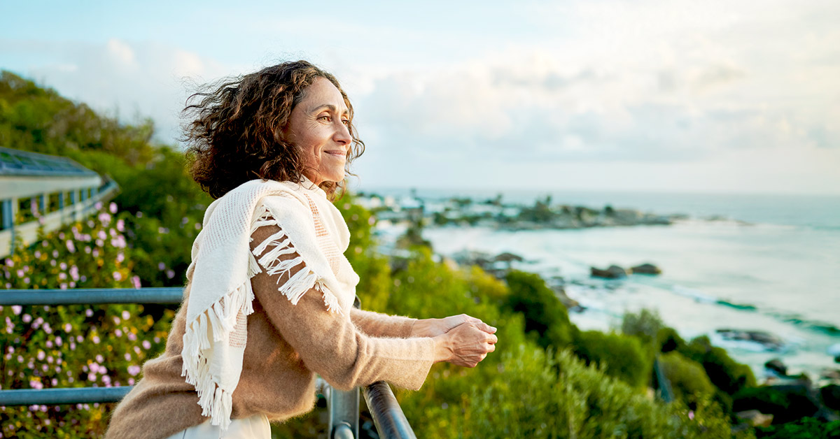 A happy woman in her 50s enjoying the outdoors overlooking the beach.