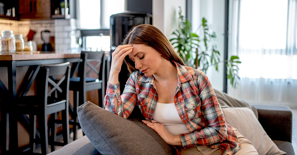 A Women sitting at home on her couch with a headache.