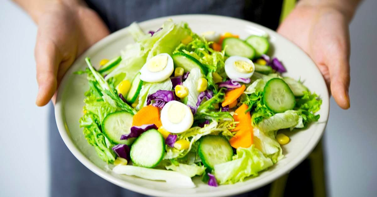 A man holding a plate with greens salad with eggs.