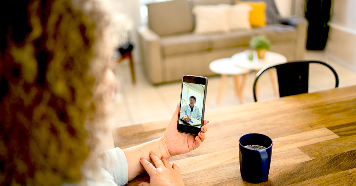 A having doctor consultation using her phone sitting at her kitchen table with a cup of coffee