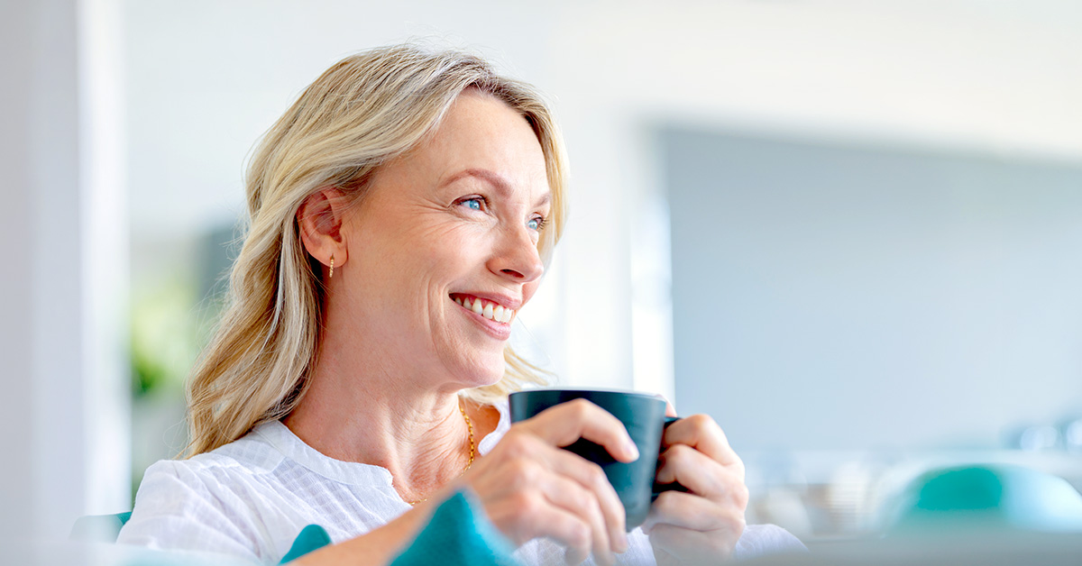 A mature and happy woman sitting on her couch holding a cup of coffee