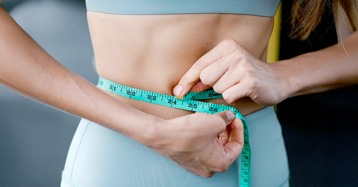 A woman measturing her weight with a measuring tape. 