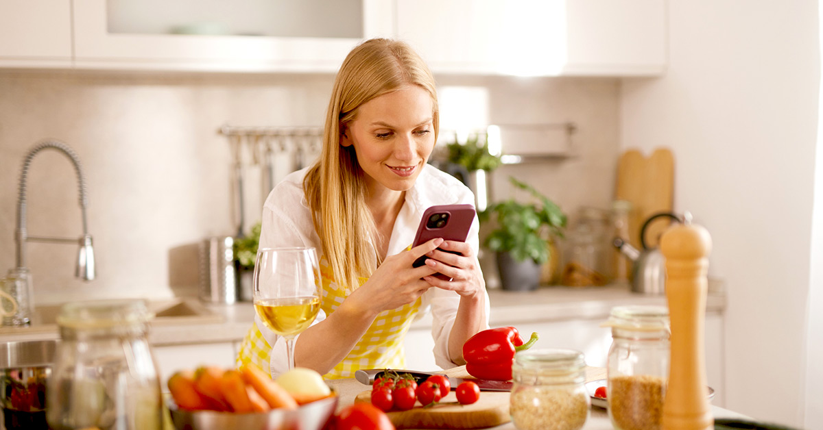 Woman checking meal-planning ideas on her phone while preparing fresh vegetables in the kitchen.