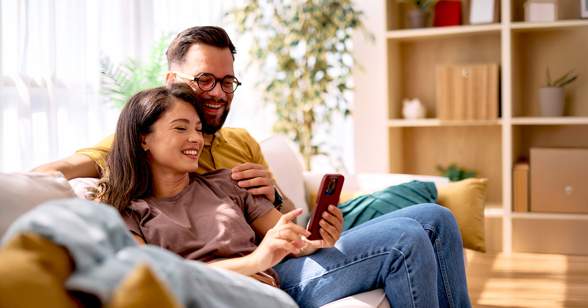 Smiling couple relaxing on a couch and looking at a smartphone together