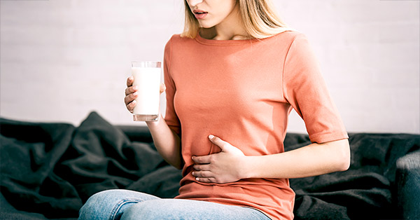 young women wearing orange is holding a glass of milk in one hand and holding stomach with the other hand due to discomfort