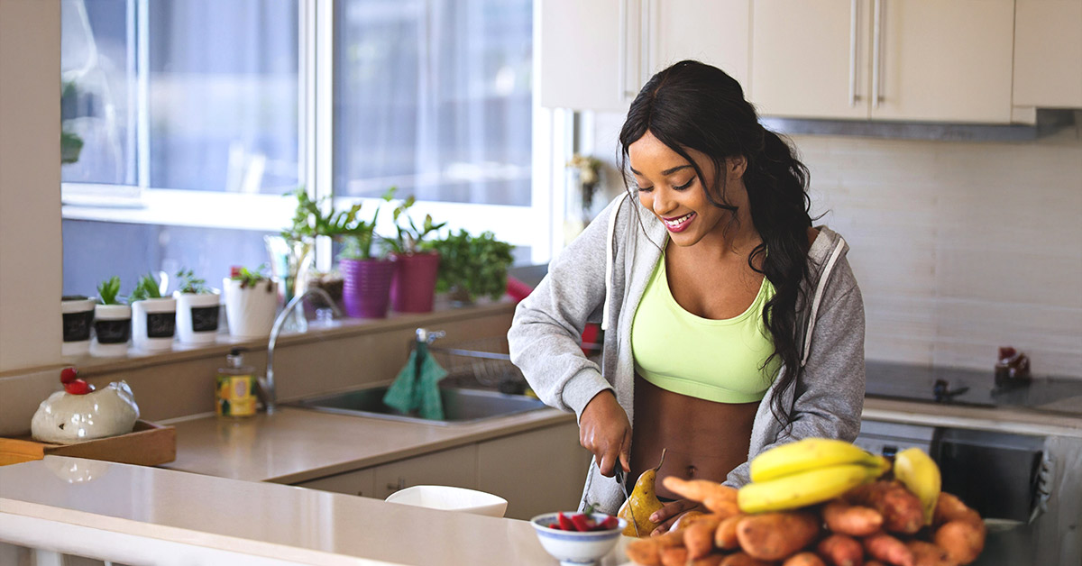 Joyful young woman cutting fruit on the counter of the kitchen.