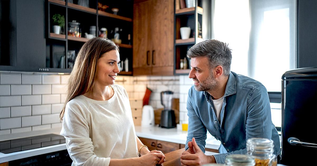 Woman and man sitting across from each other at a kitchen island, smiling during a relaxed conversation at home.