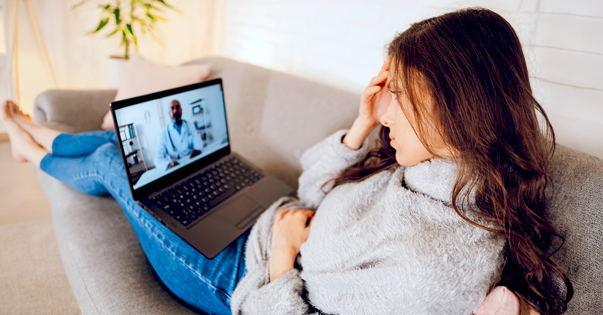 A woman sitting on couch with feet up having a telemedicine appointment with her doctor.