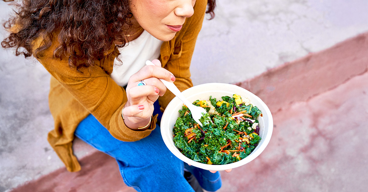 A woman sitting outside on a step eating a bowl of kale salad.