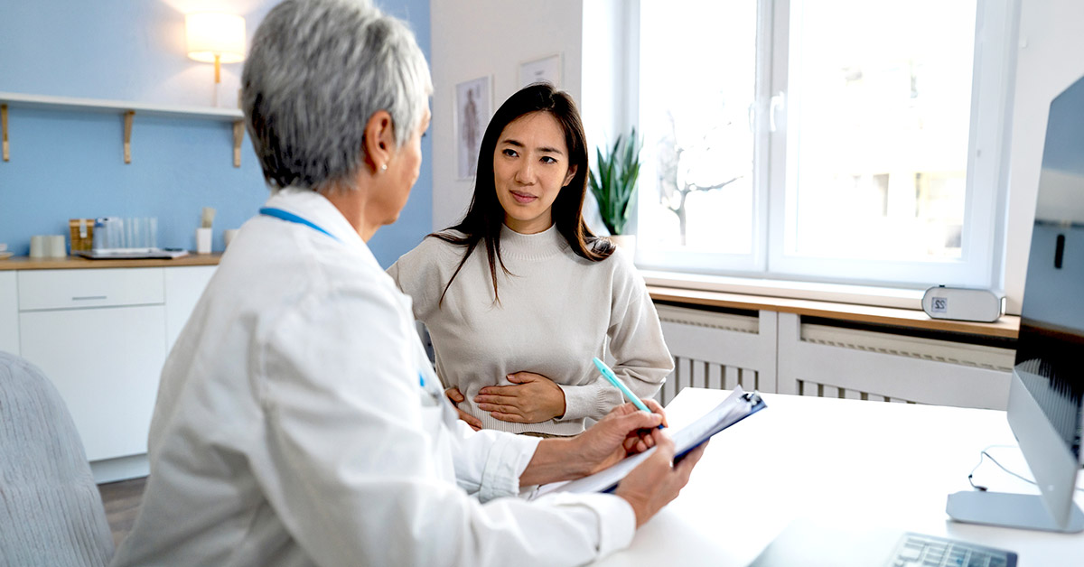 Woman holding her upper right abdomen while speaking with a doctor during a medical consultation.