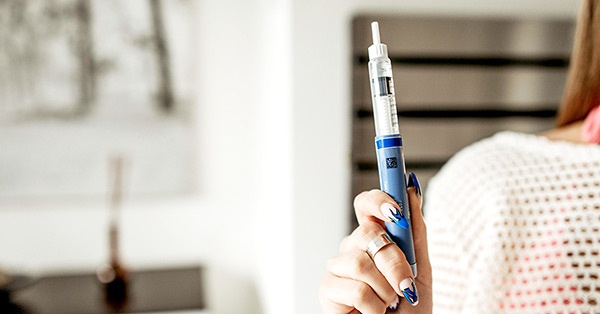 Women holding up a blue semaglutide injection in her right hand