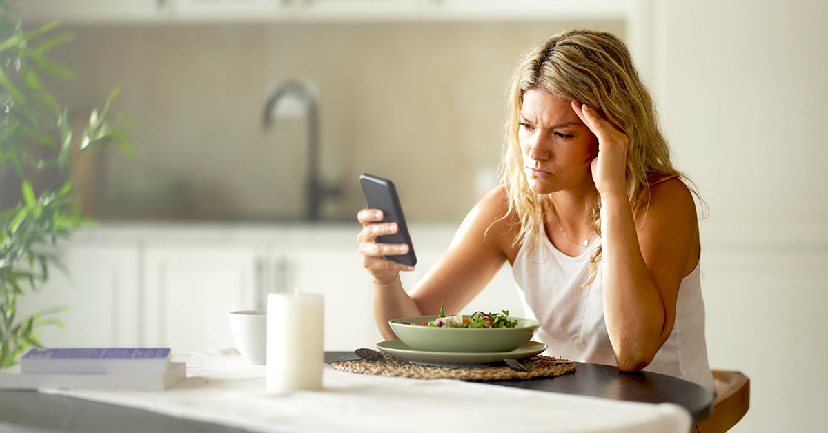 A woman upset with her meal staring into her phone at the table