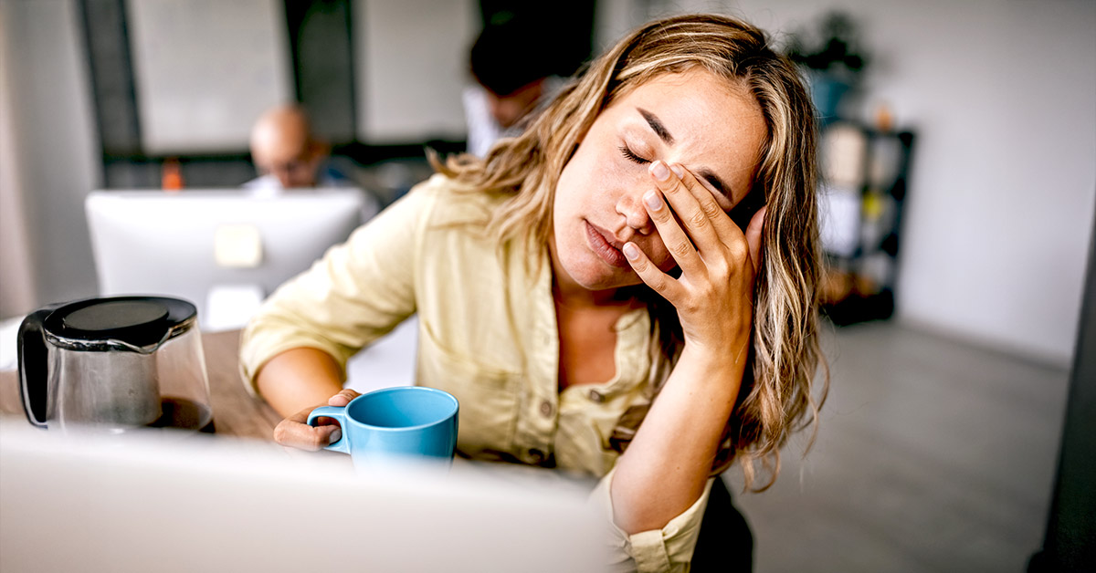 A woman with hand to the face tired and holding cup of coffee